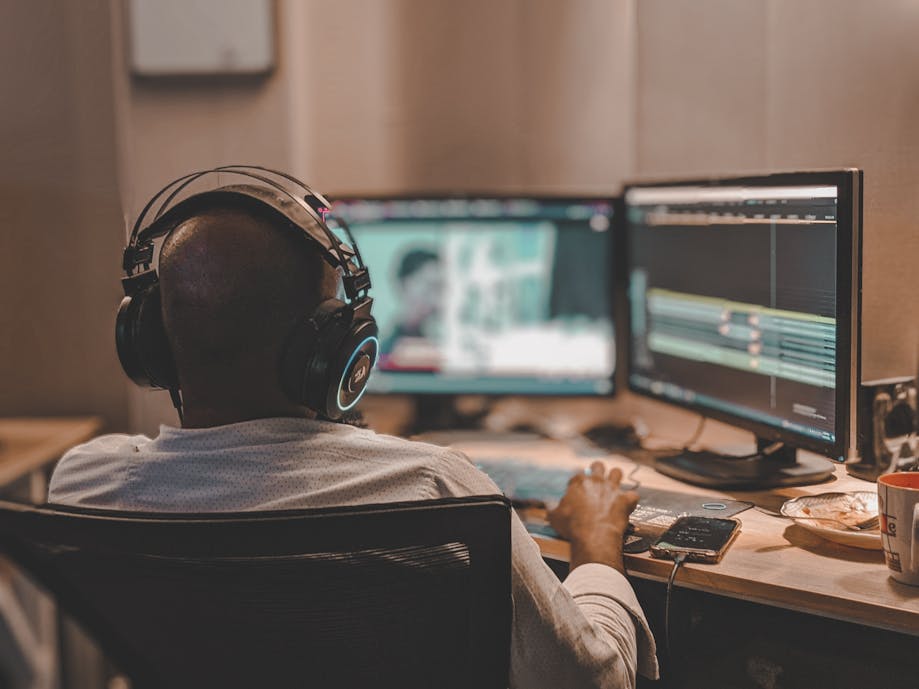 A person, embodying the essence of "what does a videographer do," wears headphones and works meticulously on video editing at a dual-monitor setup.